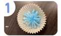 Labeled "one." A blue handmade pom pom sitting in a yellow cupcake liner.