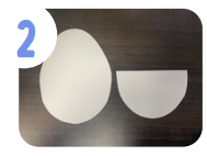 Labeled "two." An egg shape and half of an egg shape cut out of white cardstock on a brown table.