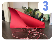 Labeled "3." A sheet of red cardstock that has been folded in half with the corners curled in has a string attached to the bottom.
