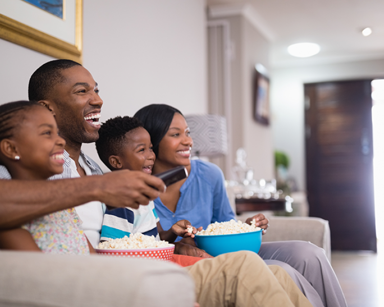 Family of four sitting on couch, eating popcorn and watching television
