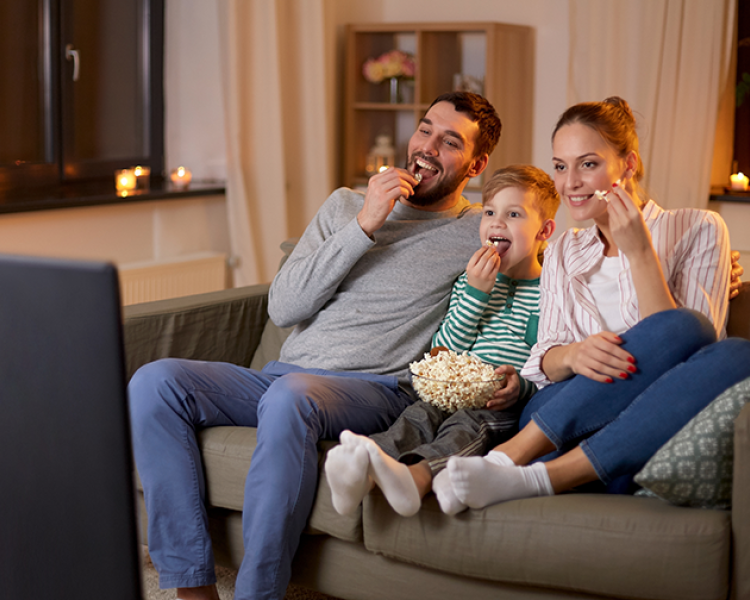 Family of three (father, mother, and son) sitting on couch, eating popcorn and watching television